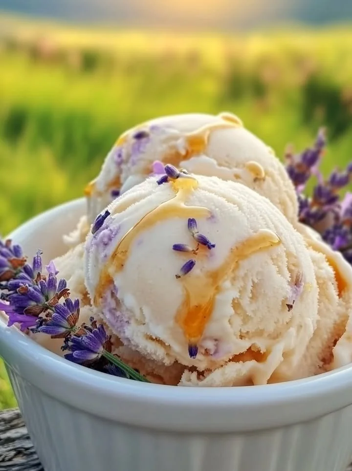 A scoop of honey lavender ice cream in a waffle cone, garnished with lavender flowers.
