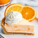 A vibrant slice of Jello Creamsicle Pie with orange and cream layers on a white plate.