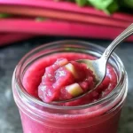 Homemade rhubarb butter in a jar with toast and fresh rhubarb stalks