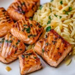 Delicious salmon bites served with lemon butter orzo on a white plate